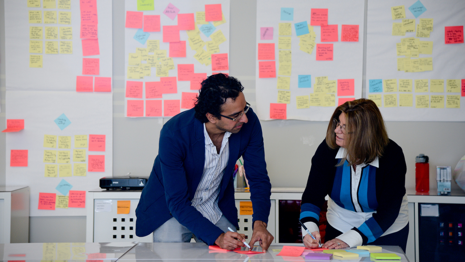 A man and woman write ideas on Post-It notes